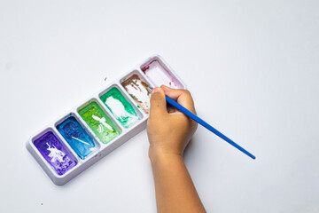 Child's hand dips brush into watercolor palette © Muhammad Azhar