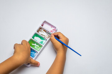 Child's hand dips brush into watercolor palette © Muhammad Azhar