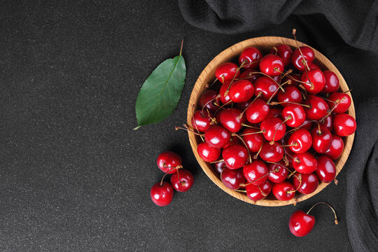 Fresh ripe sweet cherries in wooden bowl with green leaves on black textured background, copy space. Healthy organic summer fruit, juicy red berries, natural freshness, healthy eating, seasonal food