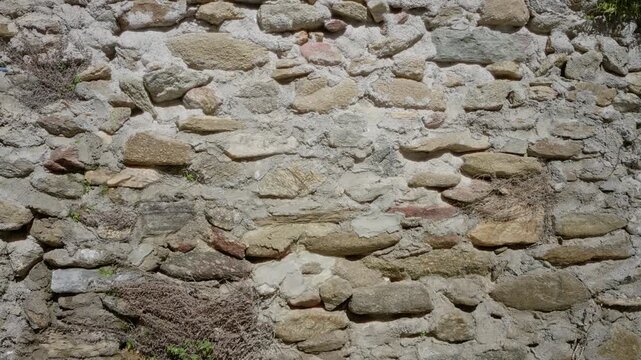 Sunlit weathered stone wall texture, sharp detailed closeup showing mortar and natural stones, exterior building; background backplate template copyspace.