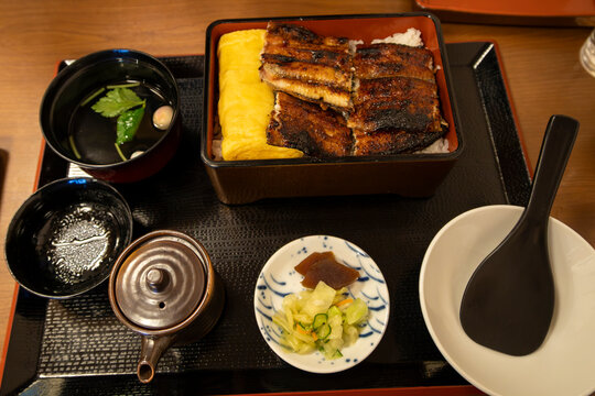 Traditional Japanese unaju set meal featuring sweet and savory glazed char-grilled unagi freshwater eel. Served alongside a thick piece of tamagoyaki omelet and rice in a lacquered box.