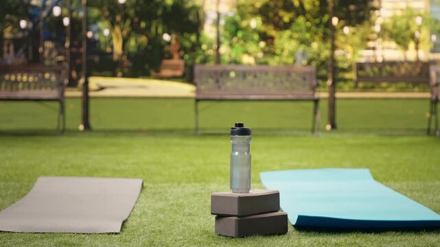 Empty city park setup with yoga brick and foam roller on a mat over grass, arranged for outdoor fitness, yoga, wellness and physical exercise.