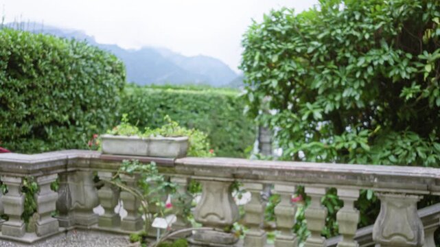 Stone balustrade and manicured hedges with lake como mountains softly blurred in shallow focus garden; background backplate copyspace calm.