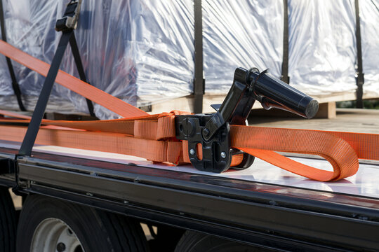 Orange ratchet straps tensioned over a wrapped freight load, cargo securing detail