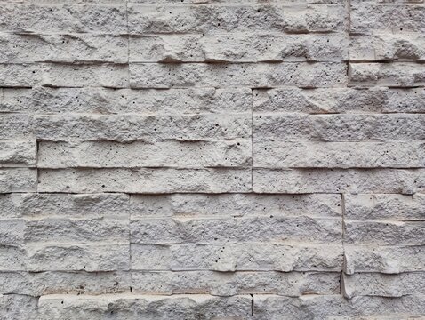 A detailed full-frame texture of modern white decorative cladding tiles mimicking rustic natural stone brickwork masonry, showcasing horizontal rows of porous rocky rectangular blocks 