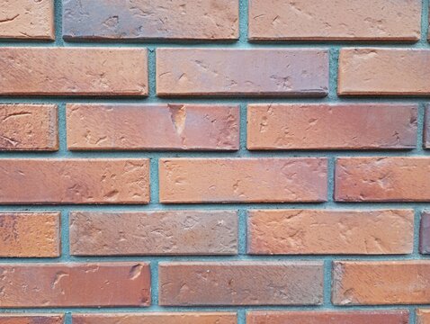 A detailed full frame texture of a modern clinker brick wall masonry showcasing rows of brown and terracotta rectangular bricks 