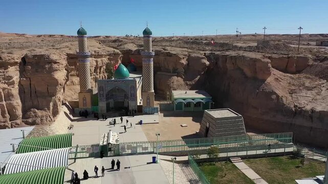 Aerial view of the Qattarat al-Imam Ali shrine with twin minarets inside a desert canyon, Karbala, Iraq