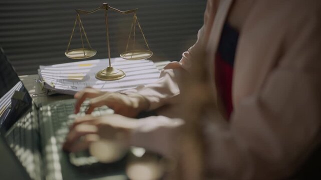 Legal professional typing on a computer beside scales of justice in a law office, representing legal research, case preparation, digital documentation, consultation, and modern legal work.