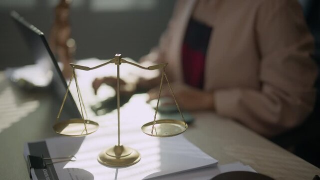 Scales of justice in focus with a legal professional working at a desk in the background, representing law, legal services, case preparation, judicial work, fairness, and professional practice.
