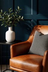 Fototapeta premium Modern reading nook with brown leather armchair, grey patterned pillow. White ceramic vase with green plant sits on small black side table. Dark blue wall creates moody atmosphere in stylish