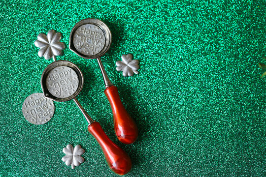 Metal Clover Molds on Glittering Green Background. Tin Pouring Set on Green Glitter Background for tin pouring instructions,holiday gift sets and New Year fortune telling activities.New Years Eve