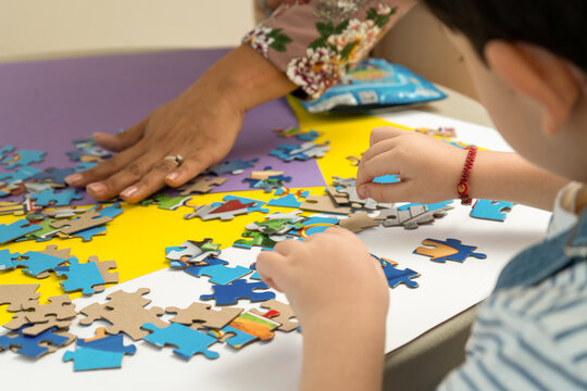 Close up of teacher helping unrecognizable child to assemble a puzzle. Early childhood education concept, guidance, learning support and teamwork
