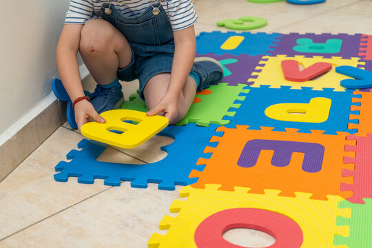 Unrecognizable kid placing foam letter into a colorful alphabet puzzle mat on the floor. Preschool literacy activity supports letter recognition and fine motor skill development in kindergarten