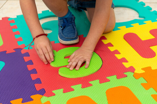 Unrecognizable kid placing foam letter into a colorful alphabet puzzle mat on the floor. Preschool literacy activity supports letter recognition and fine motor skill development in kindergarten