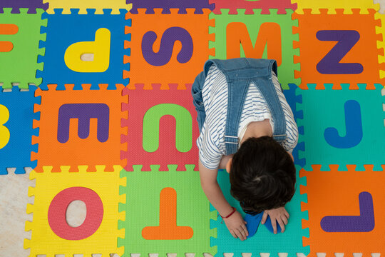 Unrecognizable kid placing foam letter into a colorful alphabet puzzle mat on the floor. Preschool literacy activity supports letter recognition and fine motor skill development in kindergarten