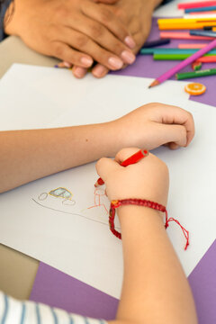 Close up of unrecognizable child hands drawing with markers, while teacher or psychologist hands support in the background. Art therapy and school psychological counseling concept