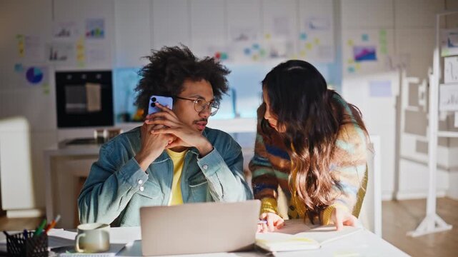Multiracial coworkers phone call. Woman pointing paperwork laptop home office.