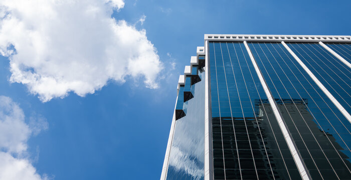 Modern Glass Office Building Against Blue Sky and White Clouds