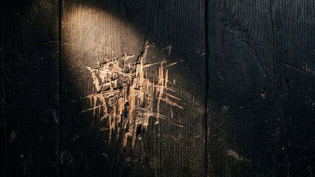 Black painted wood surface with aggressive scratch marks exposing raw timber under spotlight