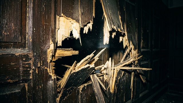 Smashed wooden door panel with a large jagged hole and flying splinters