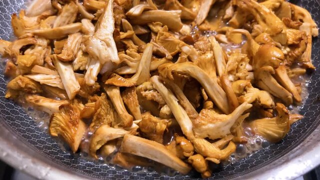Chanterelle mushrooms frying in a modern honeycomb pan as golden wild fungi simmer close-up with boiling liquid and sliced fresh elements cooking in a culinary recipe.