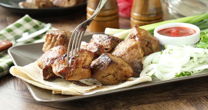 Dipping delicious shish kebab into sauce at wooden table, closeup