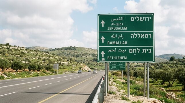 Green road sign directing to Jerusalem Ramallah and Bethlehem in Israel with a highway and hilly landscape in the background
