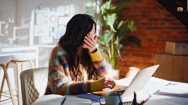 Asian woman typing laptop rubbing face loft office. Tired designer stress work.