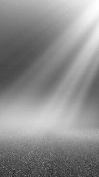 Abstract black and white background with glowing light rays shining down on a dark textured ground, creating a dramatic and mystical atmosphere. Smoke background