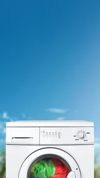 A close-up shot of a white front-load washing machine with green and red laundry inside, set against a bright blue sky background. Quotes background