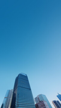 A low angle view of modern skyscrapers reaching towards a clear blue sky, capturing architectural design and urban beauty. Cityscapes or quotes background