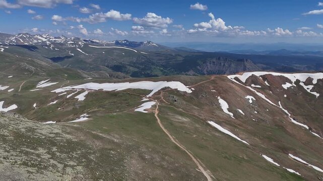 Aerial view of rolling alpine ridges with snow patches hiking trails and a small lake in Gumushane Turkey