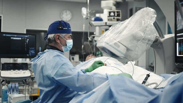 Doctor seated beside a patient monitoring an angiography procedure using medical screens.