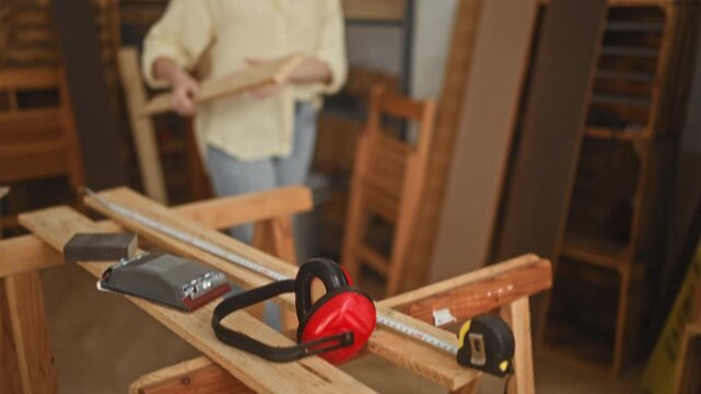 Woman carpenter holds a wooden plank with hands at a workshop workbench while smiling and aligning the board; craftsmanship confidence.
