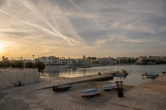 Streaked clouds and soft golden light over calm water at the harbour in Otranto, Puglia, Italy