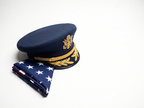 A folded American flag rests beside a military officer's cap with gold trim and an emblem.