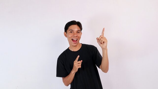 Excited young Asian man laughing with an open mouth while raising his index finger up in an eureka idea gesture against a white background.