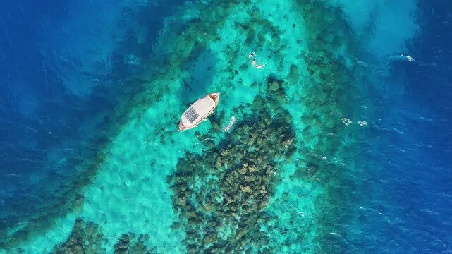 Aerial rise over rocky shallows and seagrass beds with a small boat in turquoise and deep blue sea in Marmaris Turkey