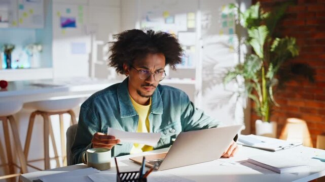 Tired employee reading document laptop office. Stressed worker rubbing forehead.