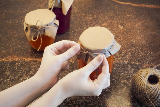 Hands decorating glass jar of homemade preserve with craft paper and twine