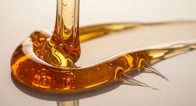 Pouring golden honey or oil stream forming smooth glossy swirls