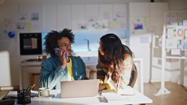 Man talking mobile phone, woman pointing laptop. Multiethnic remote work team.