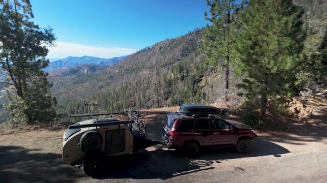 SUV with teardrop camper trailer travels through the Sierra mountains approaching Sherman Pass and passing by tall trees.