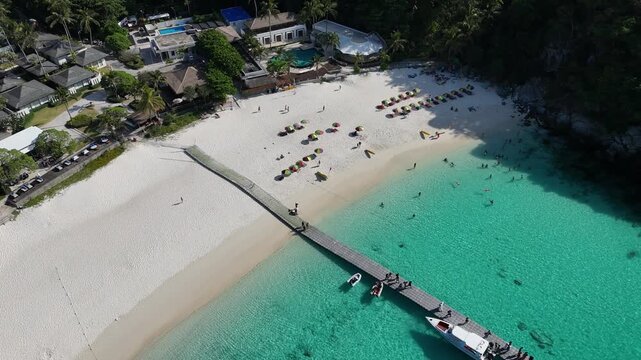 Aerial view of a long wooden pier over turquoise water at a white sand beach with sun loungers in Racha Island Phuket Thailand