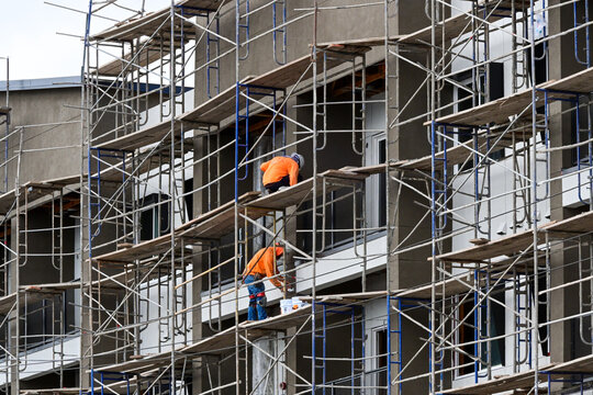 Construction workers on scaffolding install exterior components on a multistory apartment building, illustrating skilled labor, multifamily housing construction, and residential development