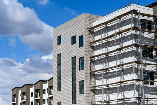 Apartment complex under construction with buildings at various stages of completion, including scaffolding and finished facades, illustrating multifamily housing development and urban growth