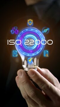 Businessman hand holding glowing lightbulb vertical shot with ISO 22000 standard hub and food icons. Food safety management system certification, hygiene compliance audit, and safe quality concept.