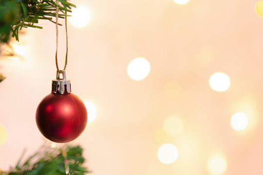Red christmas ornament hanging from green tree branch creates joyful holiday decoration with warm bokeh light background bringing cheer to seasonal celebration