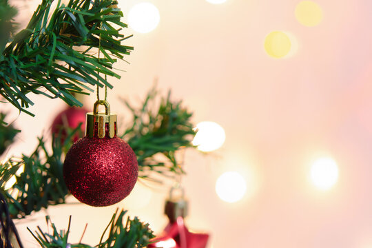 Festive red bauble ornament hanging on pine Christmas tree branch with warm bokeh light background brings joyful holiday cheer into decorated cozy room