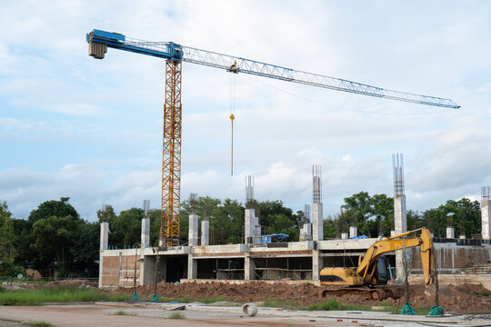 Tall crane standing above active construction site with yellow excavator machinery working on building structure showcases ambitious industry development under blue sky